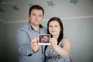 sensownipl duet fotograficzny z Krakowa. Sesja ciążowa w domu. Para wspólnie trzyma w dłońmi zdjęcie USG obrazujące maluszka.